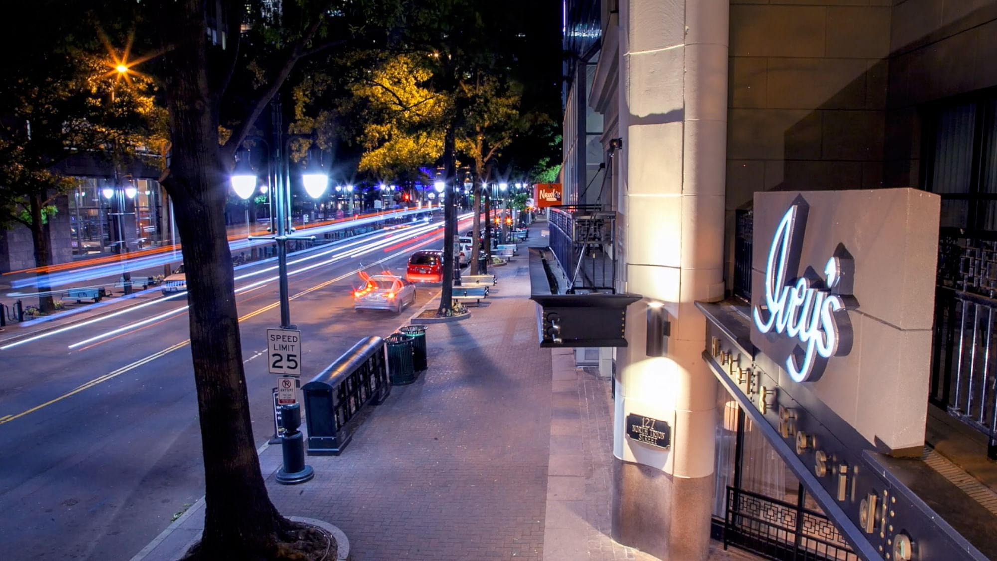 A nighttime view of a city street with a hotel sign reading 'Ivey's' on the right.