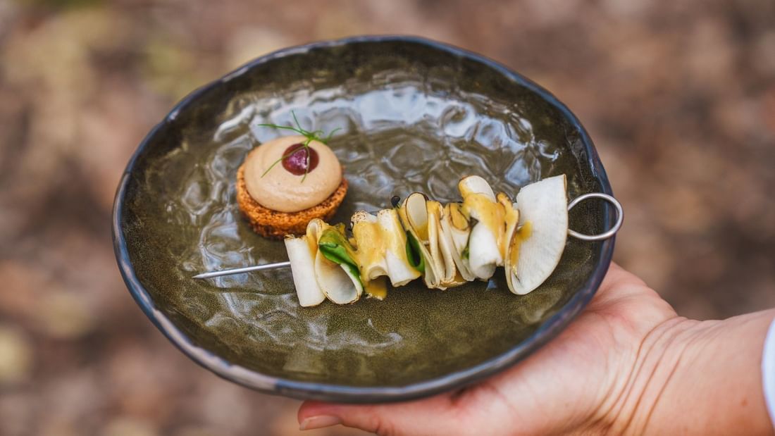 Hand holding a dark plate with gourmet appetizers including a savory tart and vegetable skewer at Pair'd Margaret River Region 2026