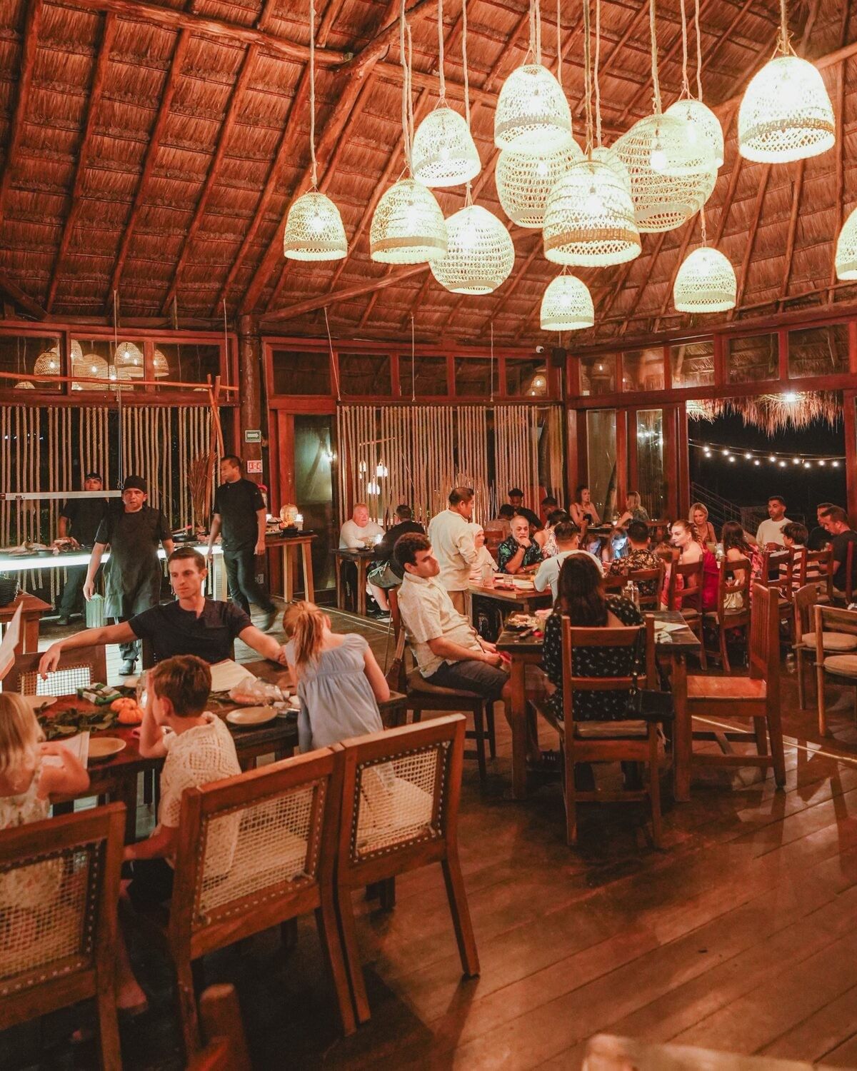 Guests sharing an evening meal around wooden tables beneath La Zebra’s palapa roof.