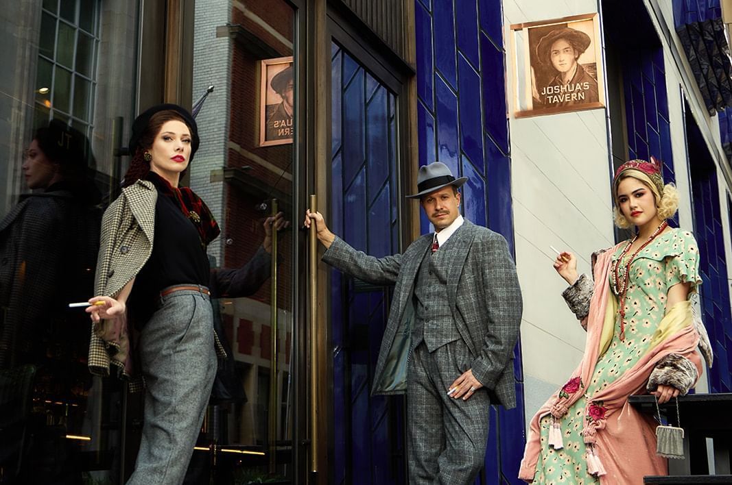 Three stylish individuals in vintage attire standing outside a building entrance, a scene from The Londoner Hotel