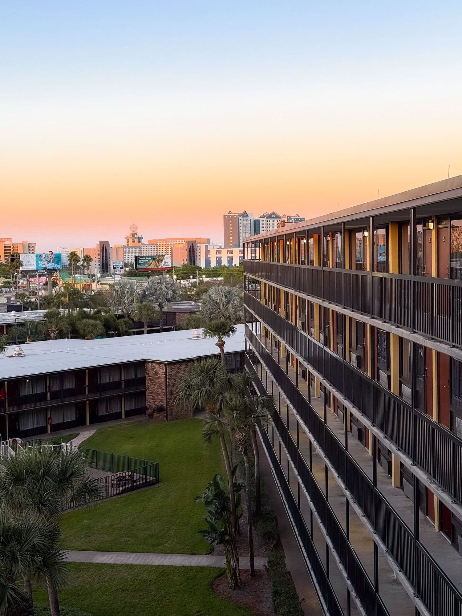 The side of a hotel with outdoor walkways overlooking other tall buildings in the distance at sunset. Enjoy summer nights in Orlando when you stay at Rosen Inn International.