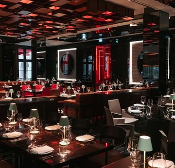 Modern restaurant interior with red and black decor, set tables, and illuminated ceiling panels at Titanic Gendarmenmarkt Berlin