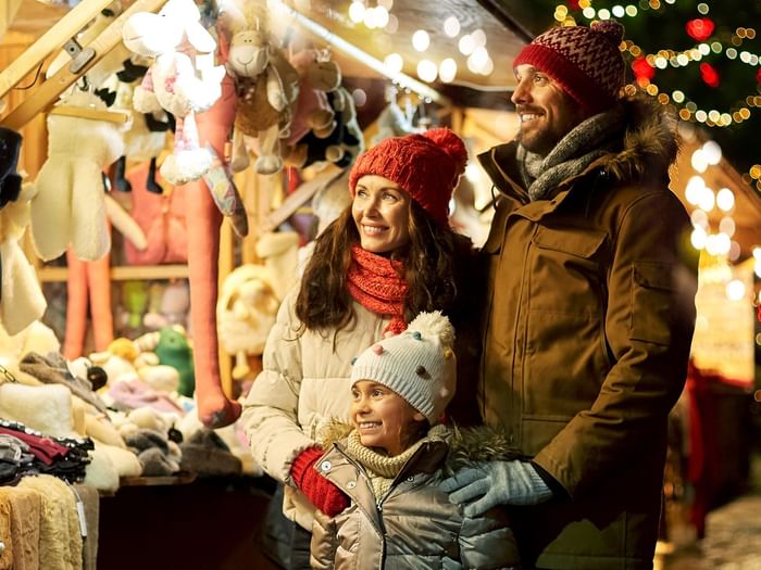 A smiling family of three stands together at a Christmas market stall.