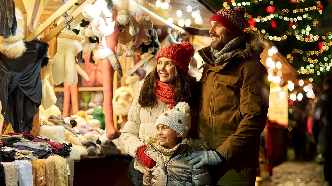 A smiling family of three stands together at a Christmas market stall.