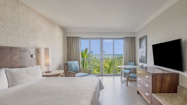 TV facing a large bed and a balcony with a palm tree and ocean views in Premium Sunset View, 1 King at Fiesta Americana