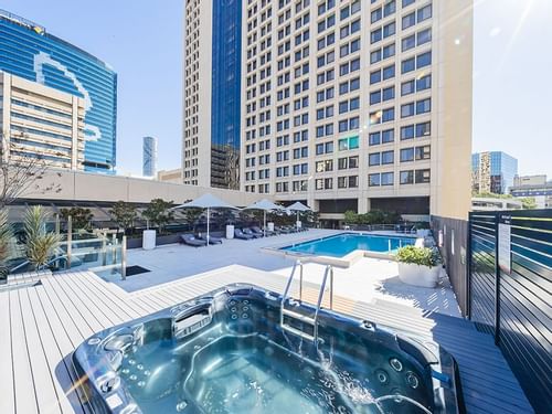 Outdoor pool area with a jacuzzi on a wooden deck, surrounded by high-rise buildings near Sofitel Brisbane Central