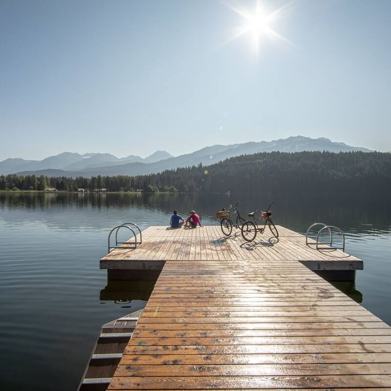 Two cyclists lounging on the deck by a lake near Blackcomb Springs Suites
