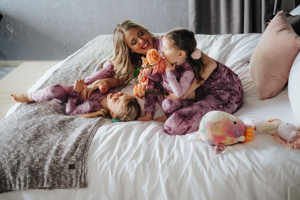 Mother and kids in matching purple pajamas laughing on a large white bed at Hotel X Toronto