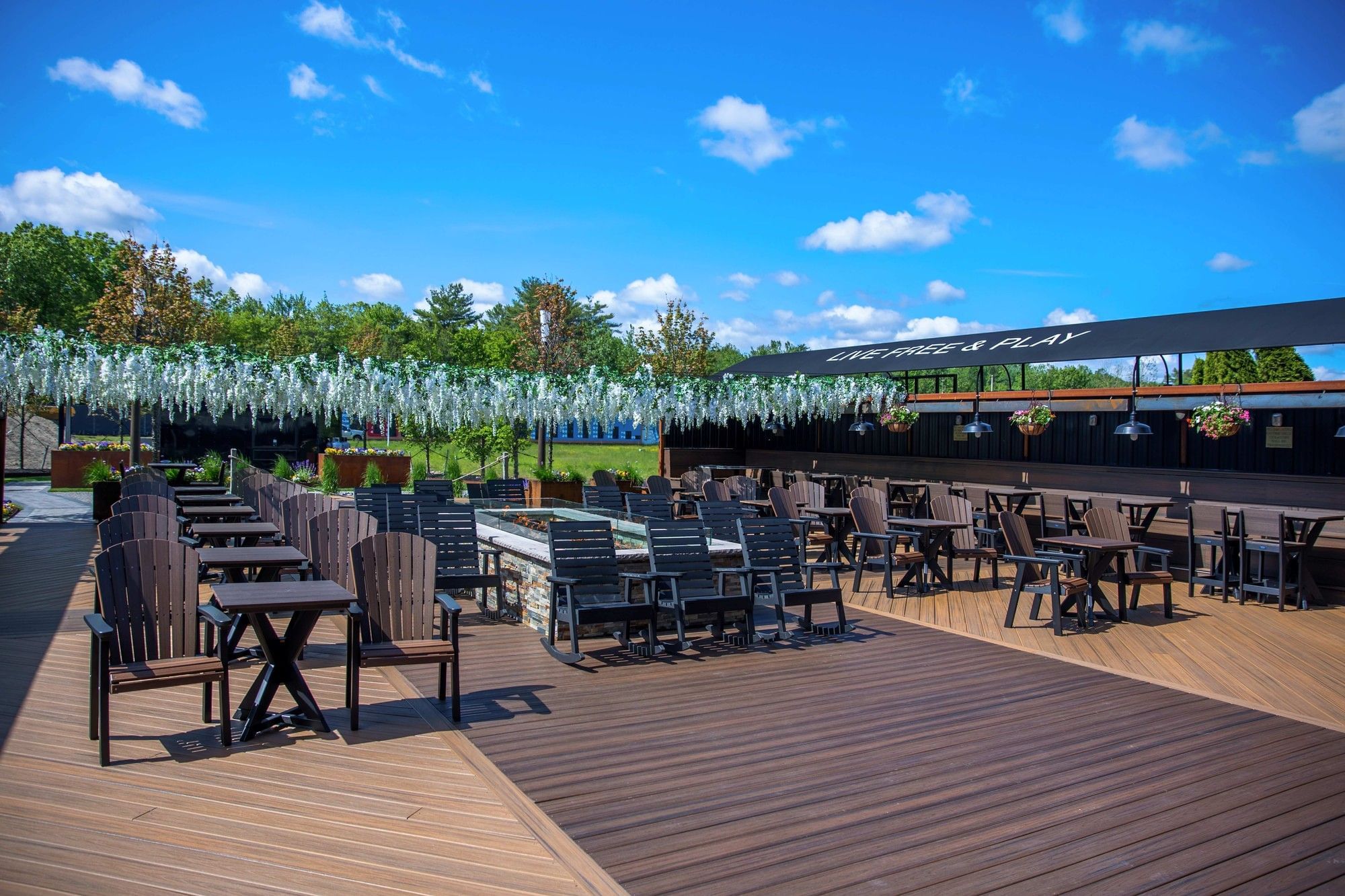 Open-air patio seating with dark wooden chairs and tables under decorative white flowers on deck venue at The Brook