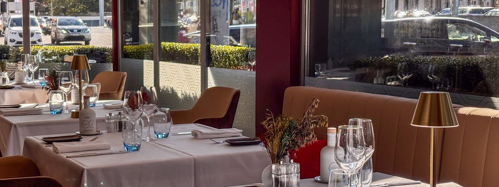 White linen tables with gold lamps by sunlit windows under a red pillar in Téséo at Warwick Geneva