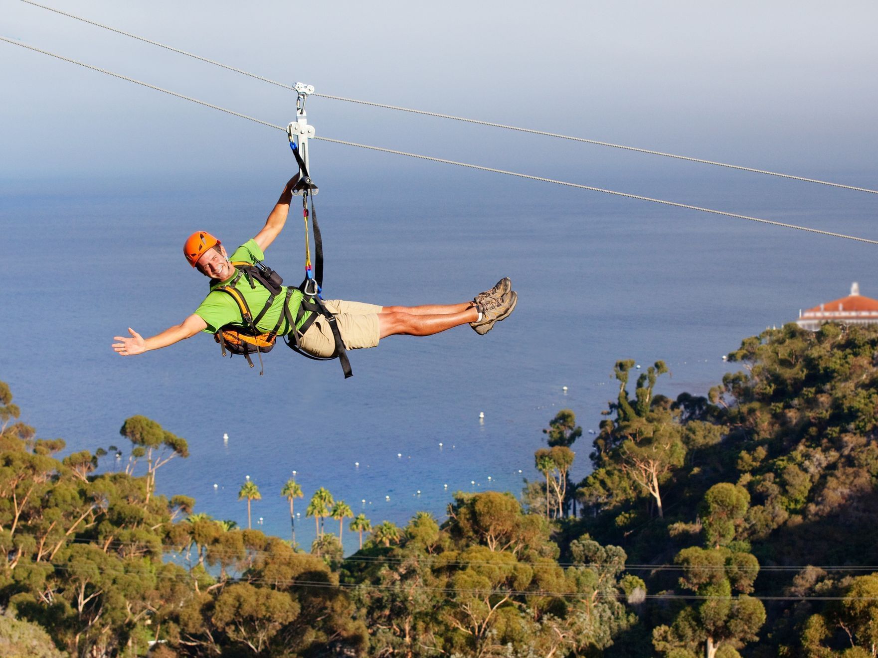 Person doing catalina island zipline over a forest with a coastal view in the background near Catalina Island Company