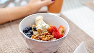 White bowl filled with healthy oatmeal porridge and fresh fruits beside an orange smoothie at Worthing Court Apartment