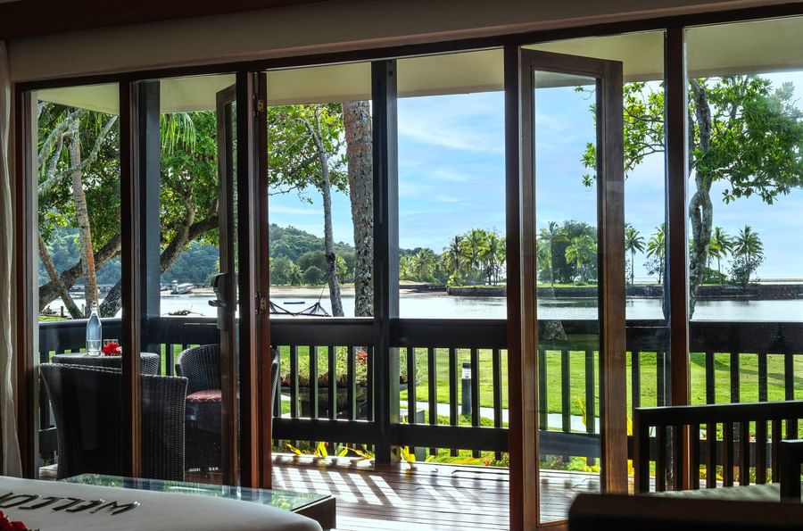 Bedroom view to balcony with water and tropical trees at The Naviti Resort Fiji