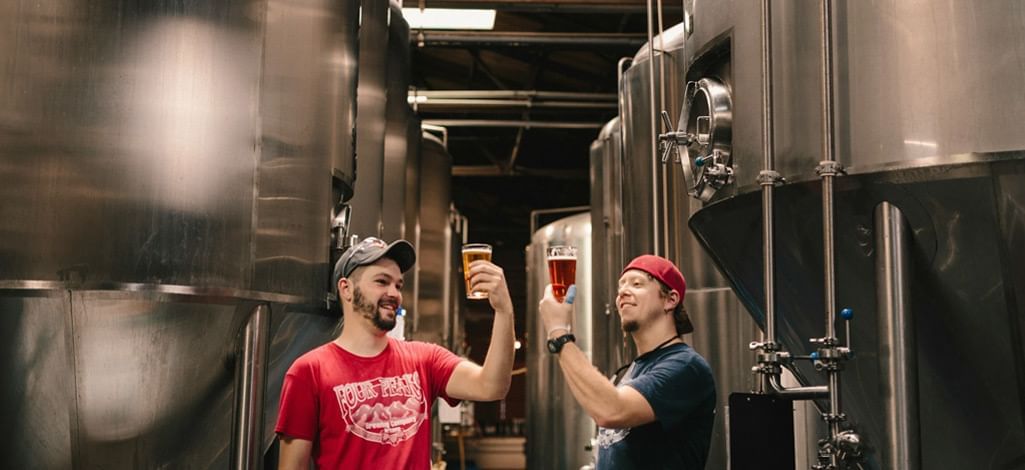 Two people sample beers near brew kettles on a Canmore brewery tour.