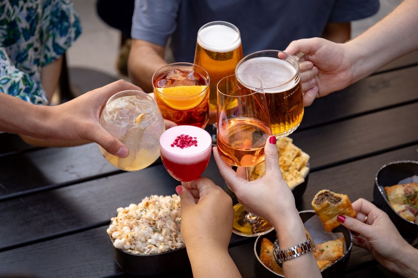 Group of friends toasting with assorted drinks and enjoying snacks on the outdoor terrace at Joshua’s Tavern in The Londoner