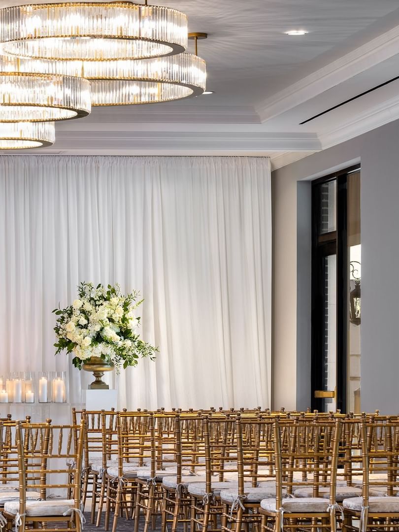 Rows of gold chairs by floral arrangements under tiered crystal chandeliers in The Foyer at Warwick Melrose Dallas