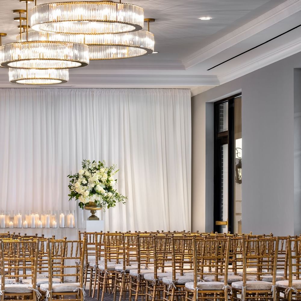 Rows of gold chairs by floral arrangements under tiered crystal chandeliers in The Foyer at Warwick Melrose Dallas