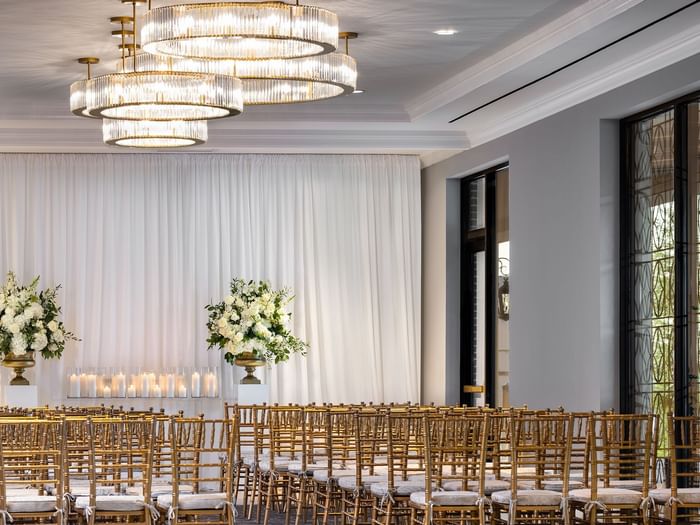 Rows of gold chairs by floral arrangements under tiered crystal chandeliers in The Foyer at Warwick Melrose Dallas