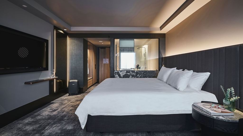 Superior room with king bed, dark upholstered headboard, wall-mounted TV, and modern bathroom at Pullman East Melbourne
