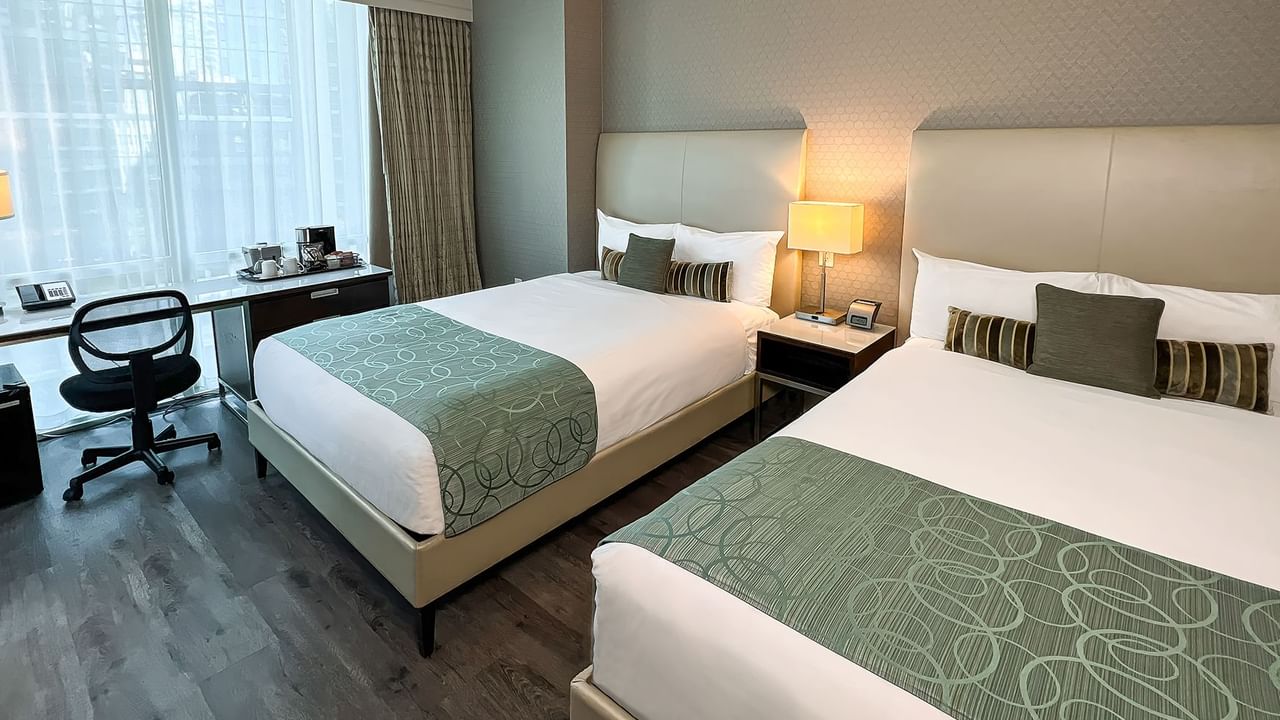 Two beds in hotel room with nightstand, lamp, table, and chair