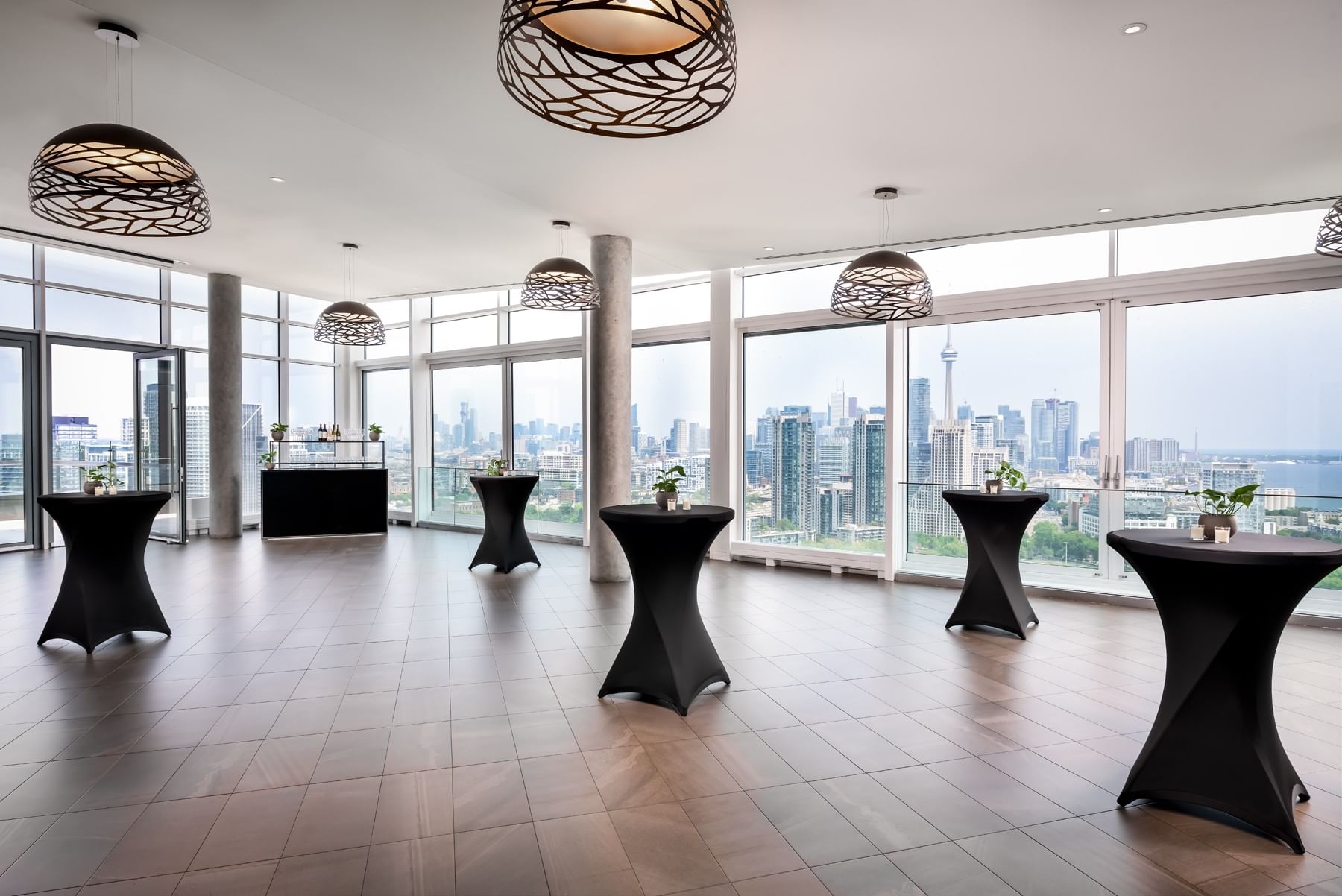 Black tables arranged under pendant lights by tall windows overlooking downtown in The View at Hotel X Toronto