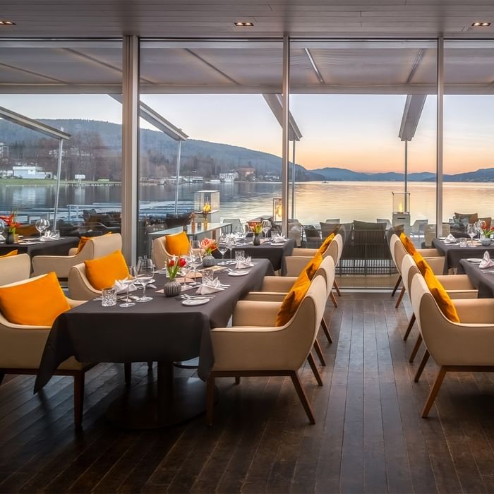 Elegantes Restaurant mit Seeblick, Tischen und Stühlen, dekoriert mit Blumen und Gläsern.
