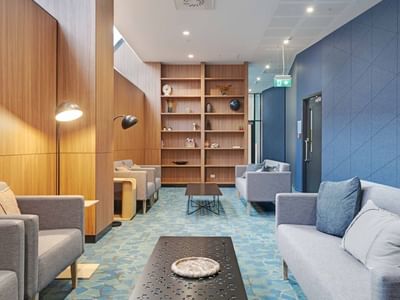 Modern lobby with gray sofas, wooden shelving, blue patterned carpet, and blue accent wall at UniLodge Auckland Central.