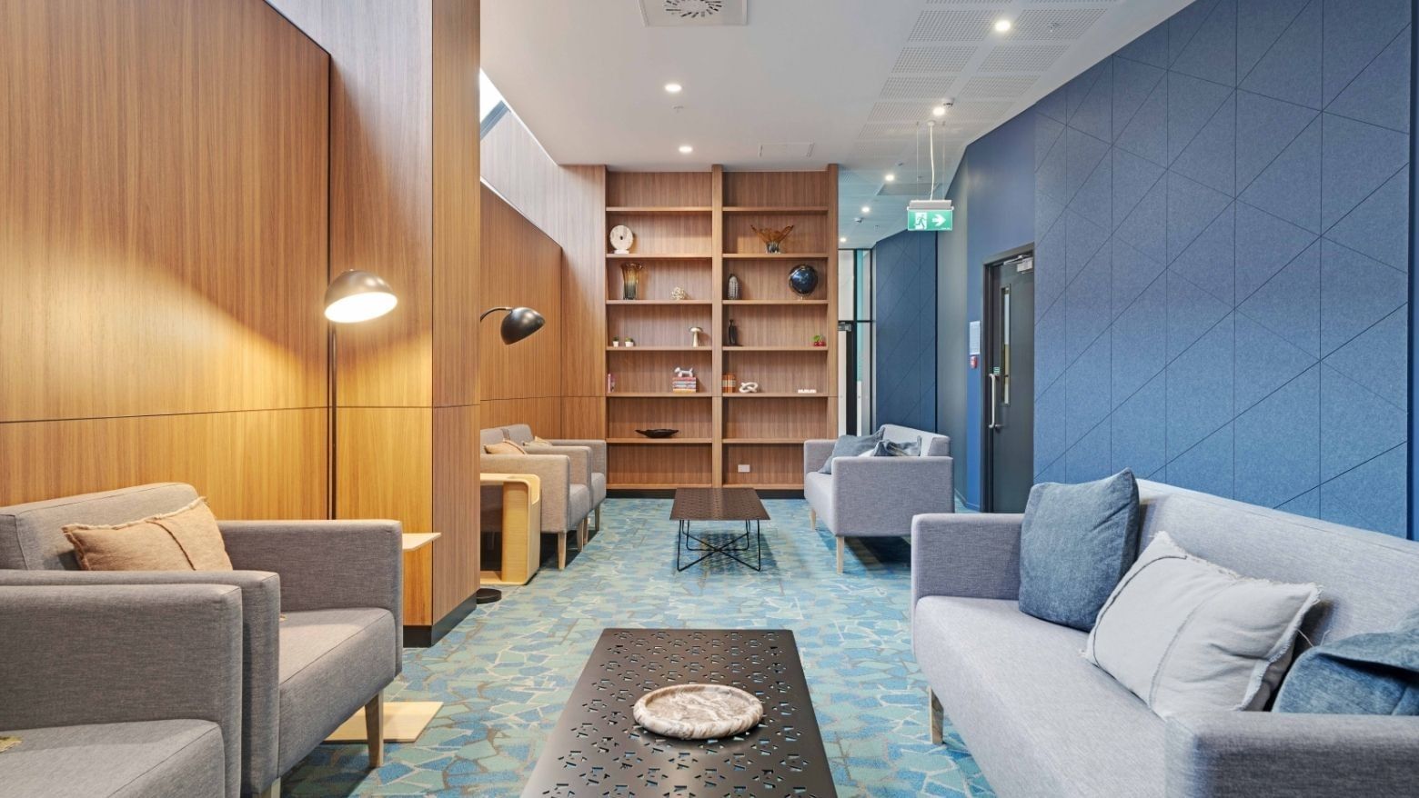 Modern lobby with gray sofas, wooden shelving, blue patterned carpet, and blue accent wall at UniLodge Auckland Central.