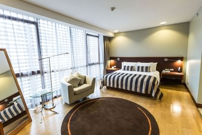 Deluxe King con cama a rayas, alfombra redonda, sillones y ventanales de piso a techo en NOI Vitacura