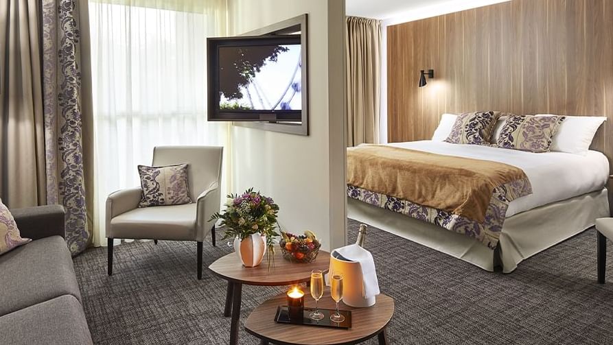 Elegant hotel room with couch, chairs, coffee table, TV, and large bed with decorative pillows.