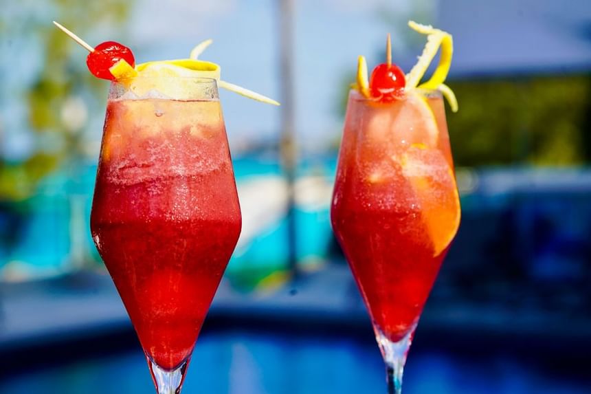 Two chilled red frozen cocktails garnished with cherries and lemon twists poolside at The Abidah Hotel by Accra