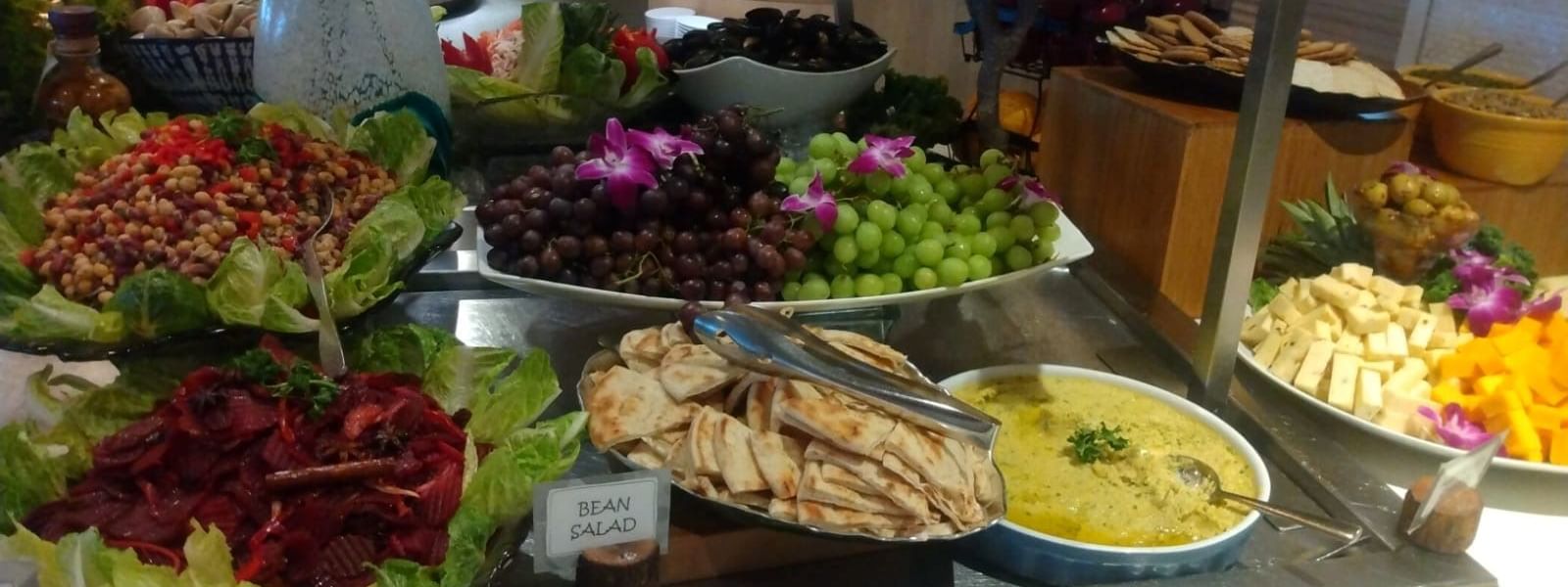 Buffet table displaying various salads, fruits, and dips with utensils and decorative flowers at Warwick Hotels and Resorts