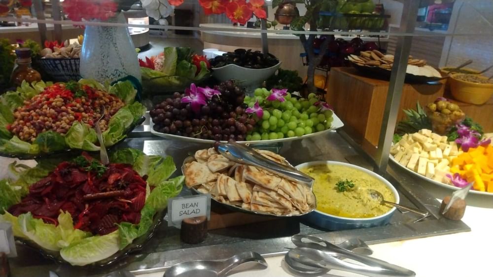 Buffet table displaying various salads, fruits, and dips with utensils and decorative flowers at Warwick Hotels and Resorts