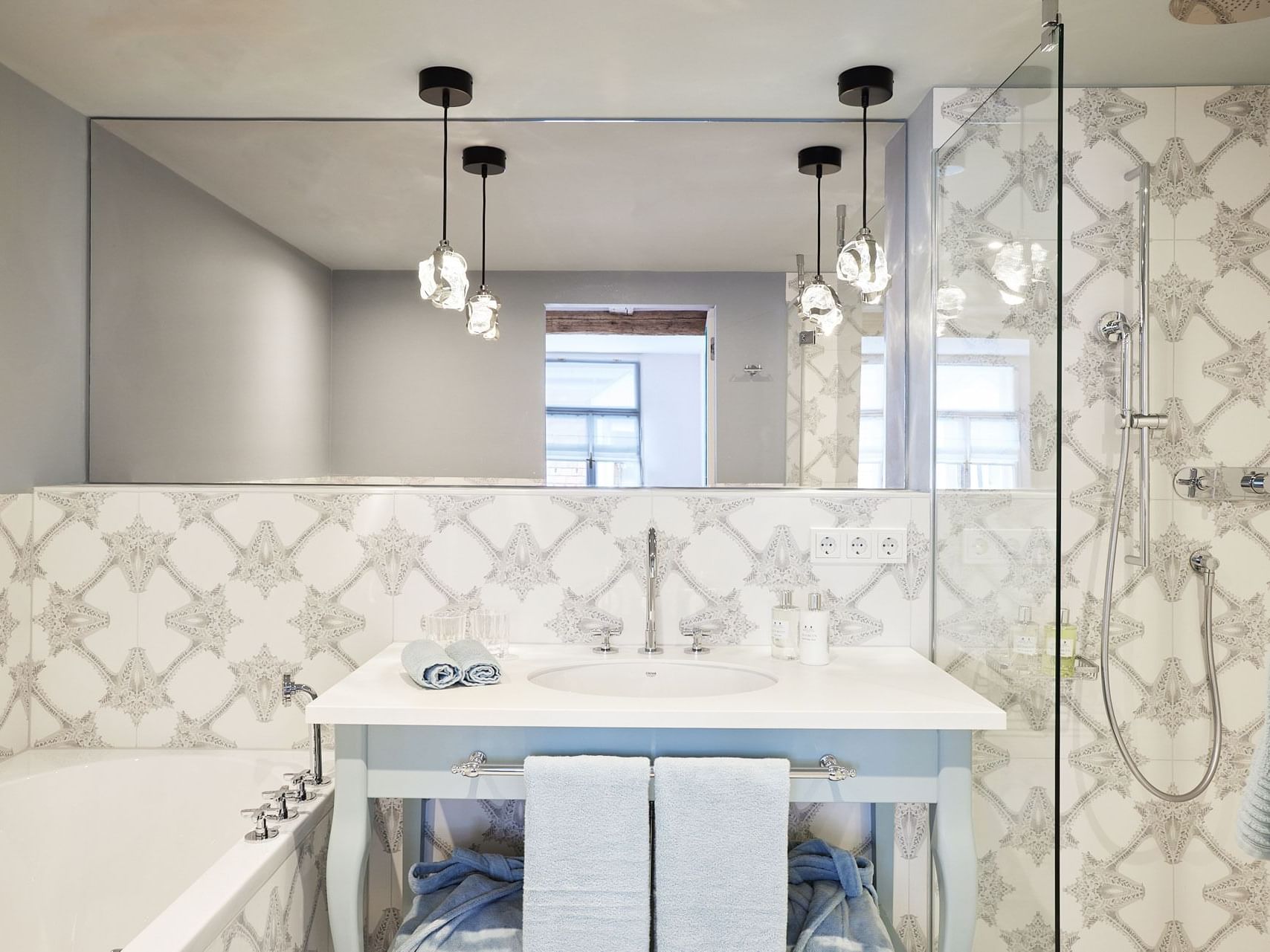 A bathroom with a sink, mirror, bathtub, and shower stall with decorative tiles and hanging towels.