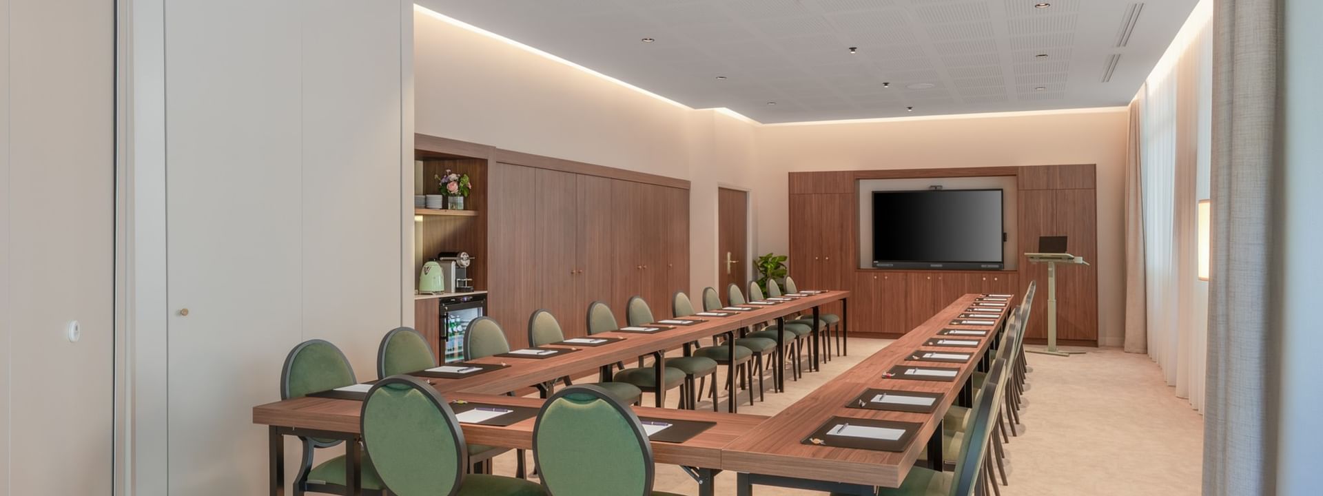 U-shaped table with green cushioned chairs and a wall-mounted TV in the Warwick meeting room at Warwick Reine Astrid - Lyon