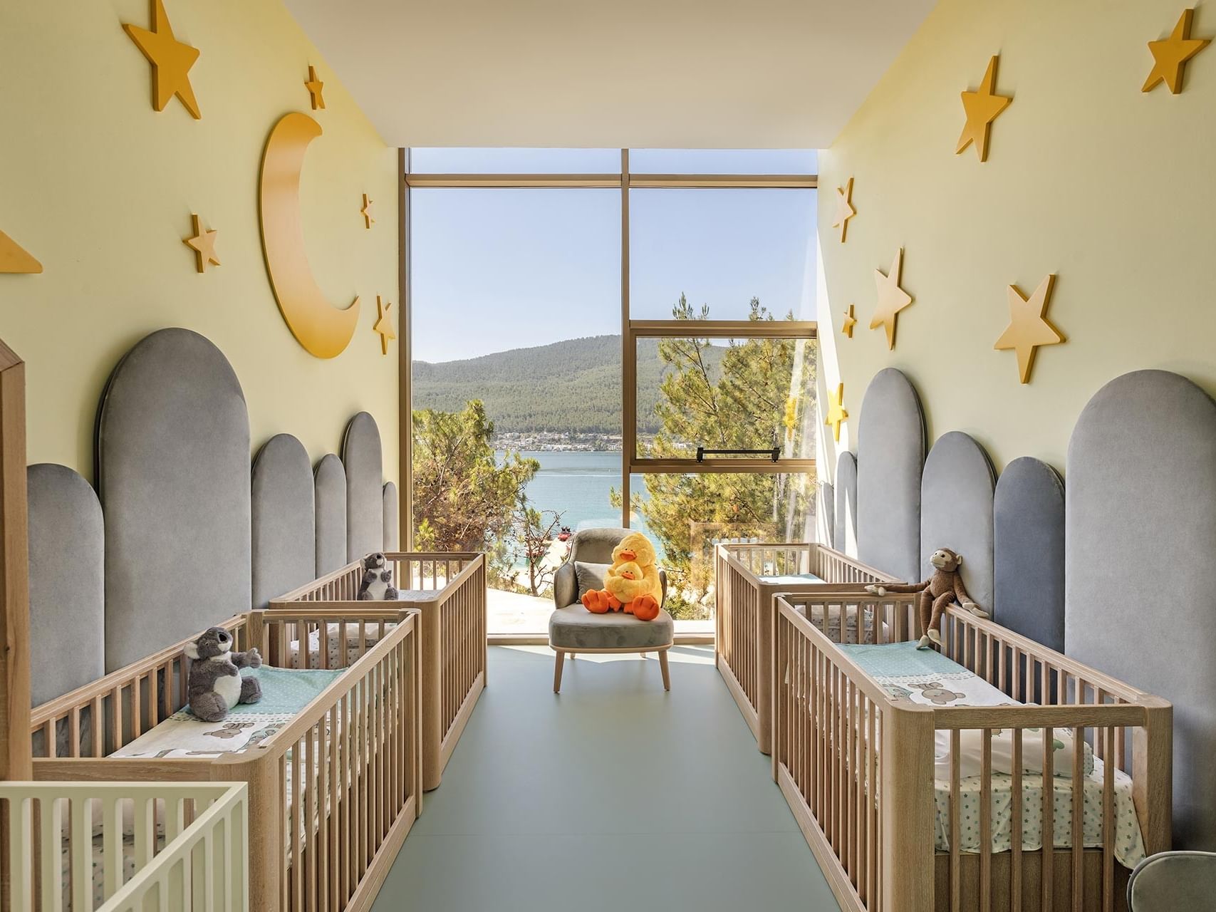 A serene baby room at Titanic Luxury Collection Bodrum, featuring large sea-view windows, cribs, and moon-and-star themed décor.