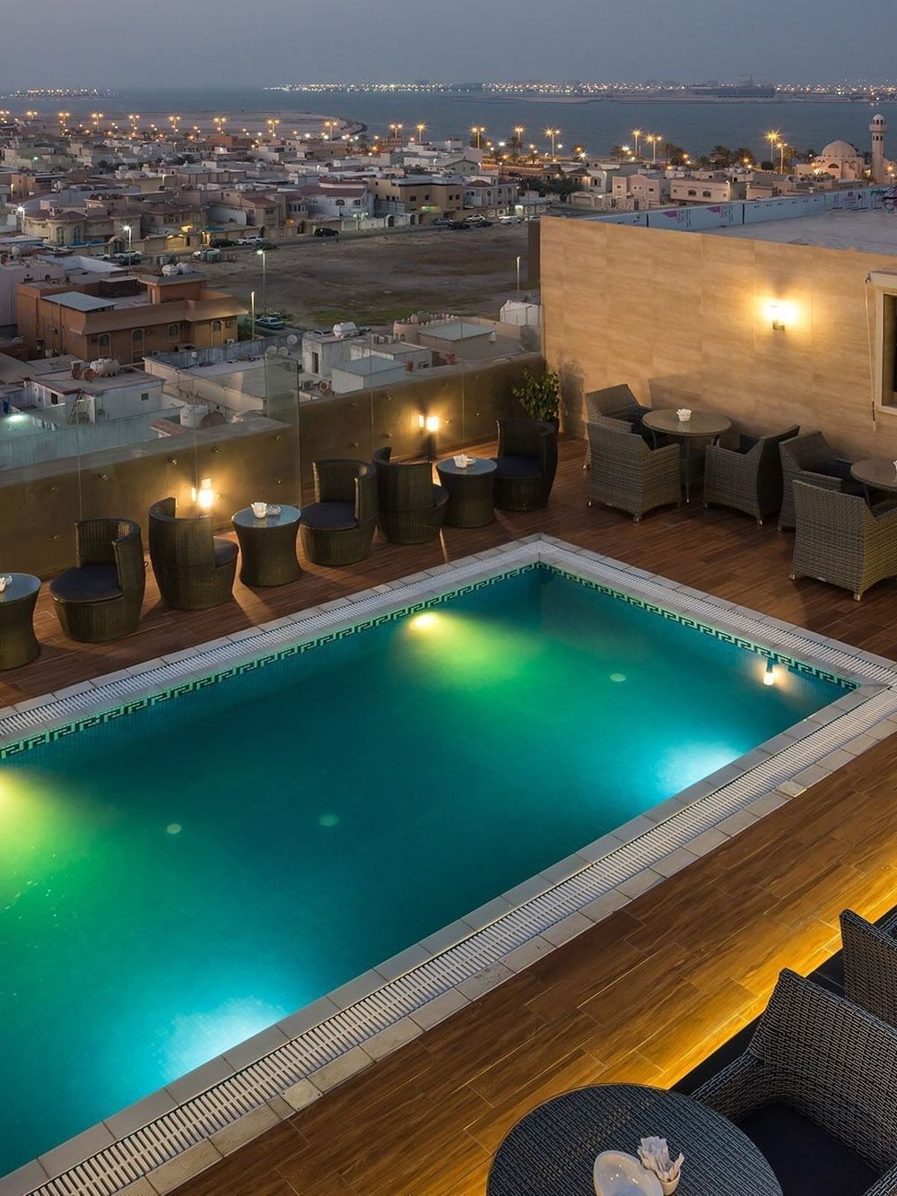 City view by rooftop pool, featuring wicker chairs surrounding tables in Sky View Café Naviti By Warwick Dammam