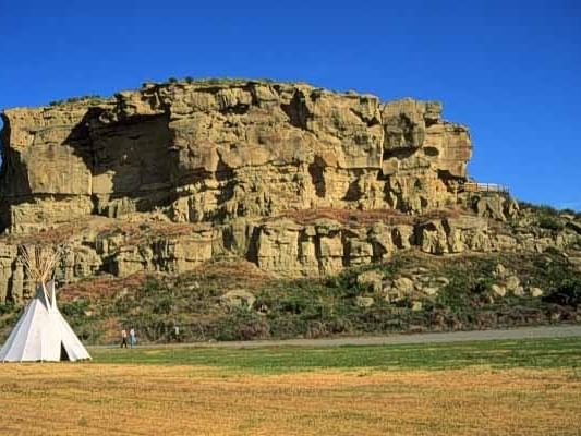 Large sandstone rock formation with layered cliffs and a white teepee in the foreground at Pompey's Pillar National Monument.