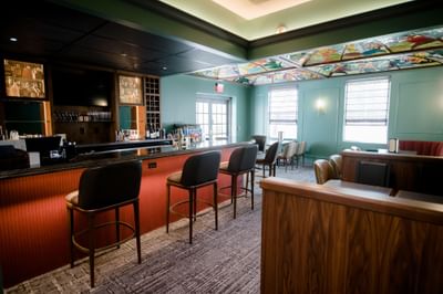 Bar counter with high stools and stained glass ceiling panel facing seating area at La Tourelle Hotel and Spa