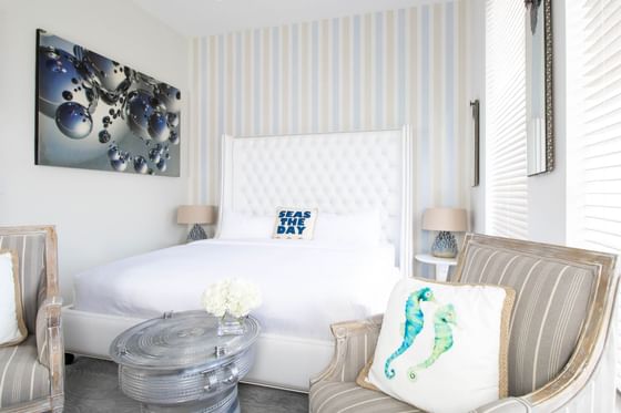 King bed with padded headboard & comfy chairs by a cozy bed in King Premiere Palm at Retro Suites Hotel