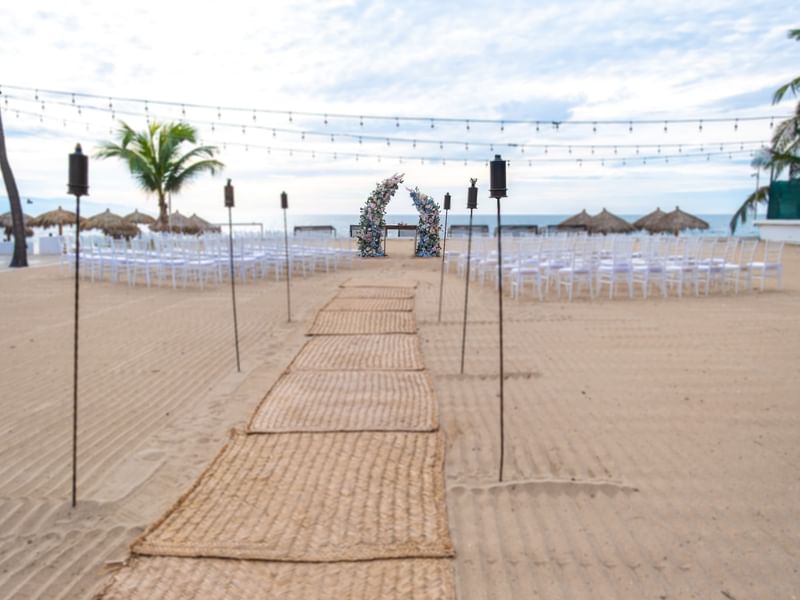 Decorated beach wedding ceremony area with chairs and floral arch at Fiesta Americana Riviera Nayarit Resort & Spa.