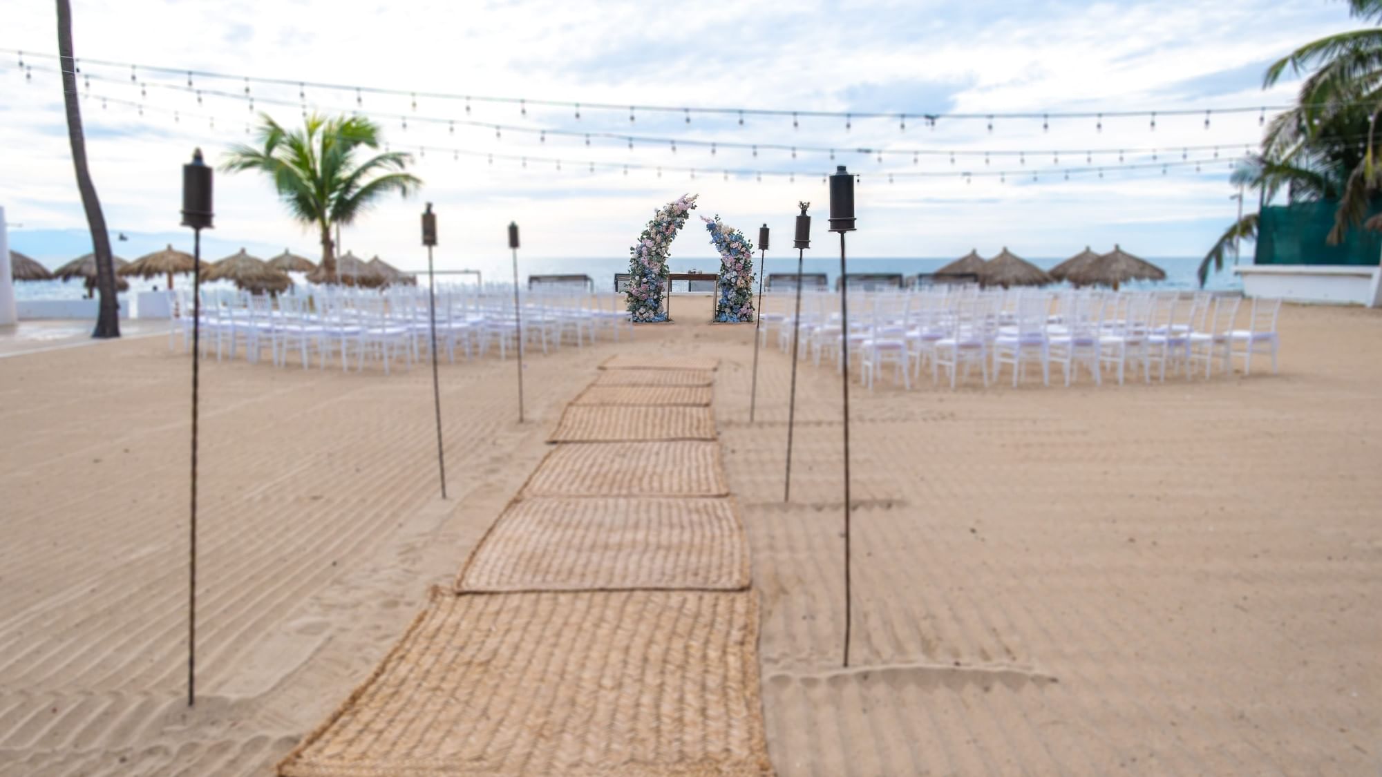 Decorated beach wedding ceremony area with chairs and floral arch at Fiesta Americana Riviera Nayarit Resort & Spa.