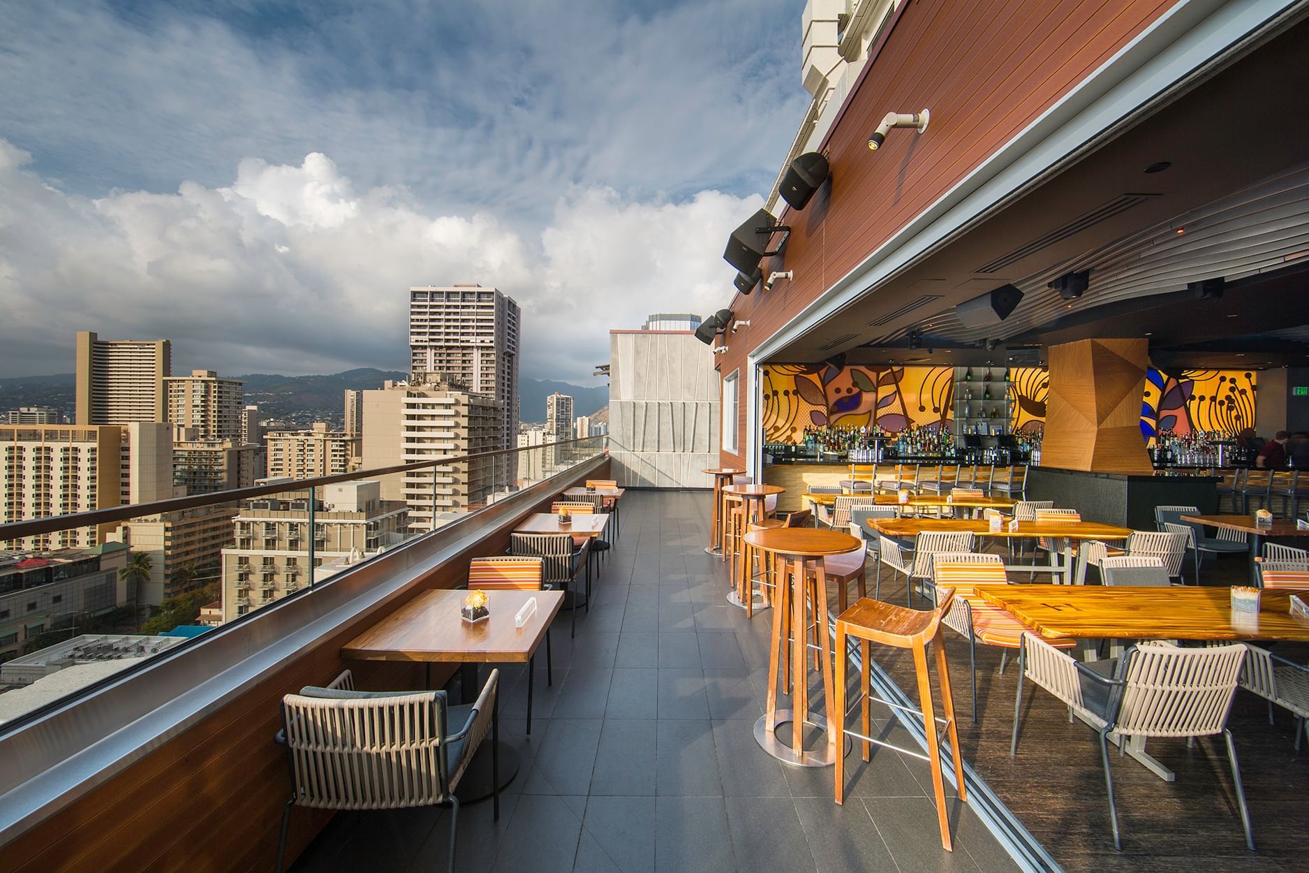 A rooftop bar with outdoor seating and a city view