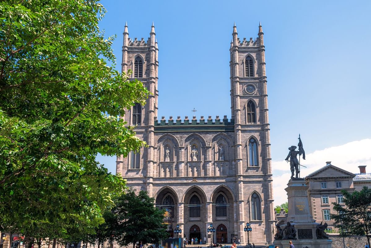 Facade of the Notre-Dame Basilica with twin towers and a statue out front at Warwick Le Crystal Montreal