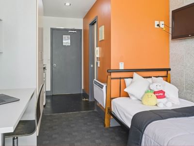 Bedroom with bed, desk, laptop, TV, and toys at Student Living Auckland - Beach.