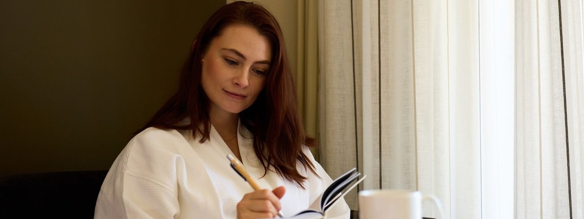 Woman relaxing with a book and coffee on a desk, promoting Stay Dine & Unwind offer.