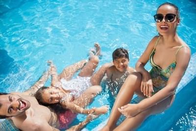 Family of four enjoying a sunny day together in a bright blue swimming pool at Playa Los Arcos Puerto Vallarta