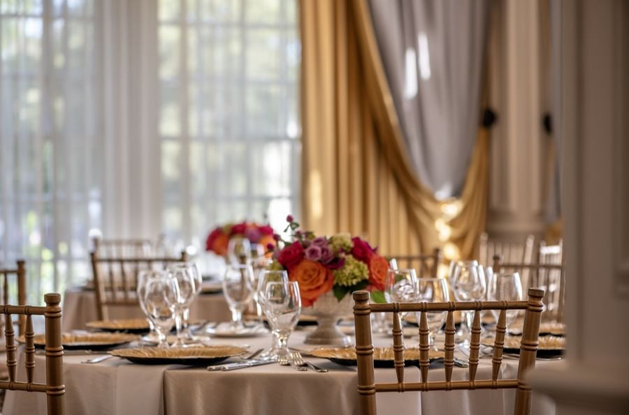 Round dining tables with gold chairs under a vibrant floral centerpiece in Crystal Ballroom at Warwick Melrose Dallas