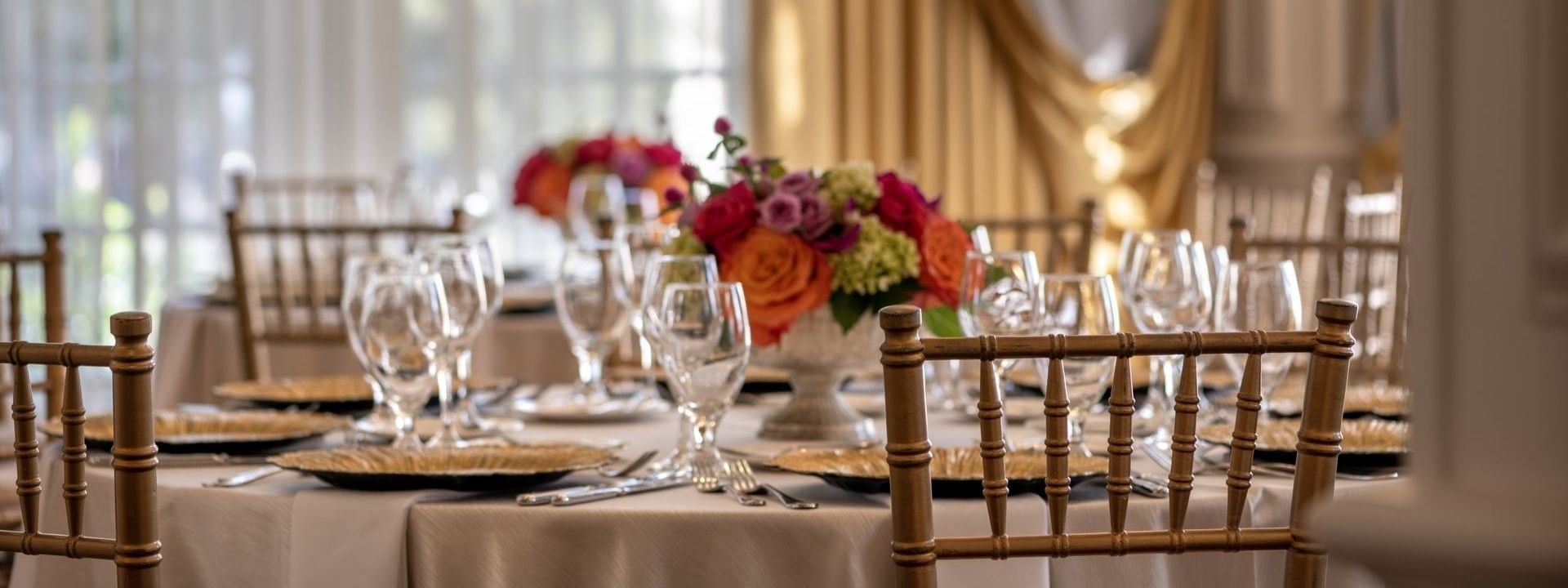 Round dining tables with gold chairs under a vibrant floral centerpiece in Crystal Ballroom at Warwick Melrose Dallas