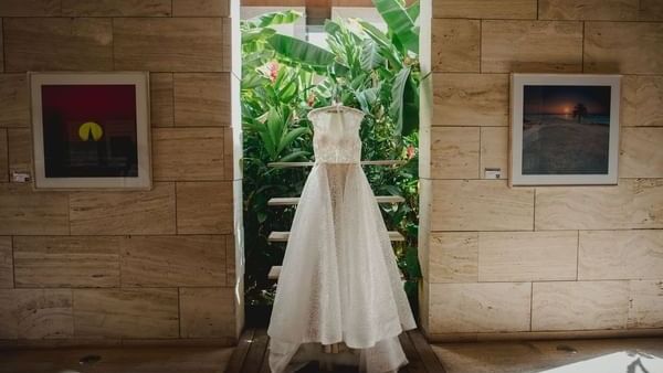 White lacy wedding dress hanging in an archway with lush green plants in the backdrop at The Explorean Resorts